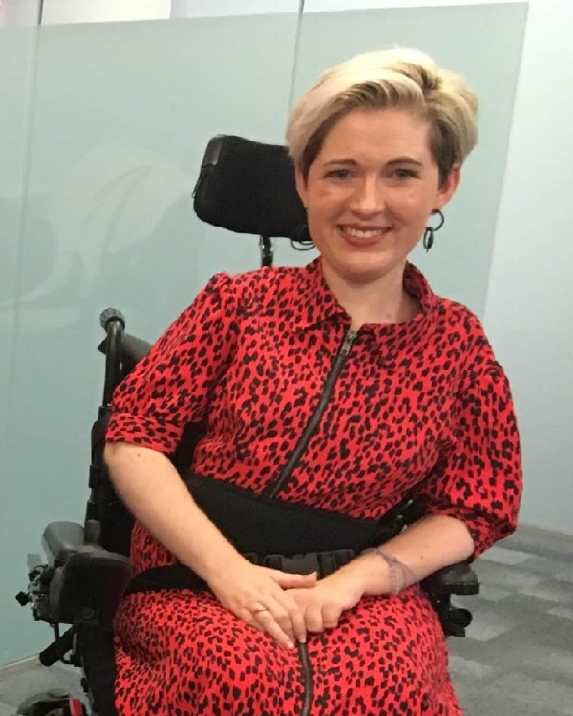 Woman in black and orange jumpsuit sitting in a wheelchair and smiling 
