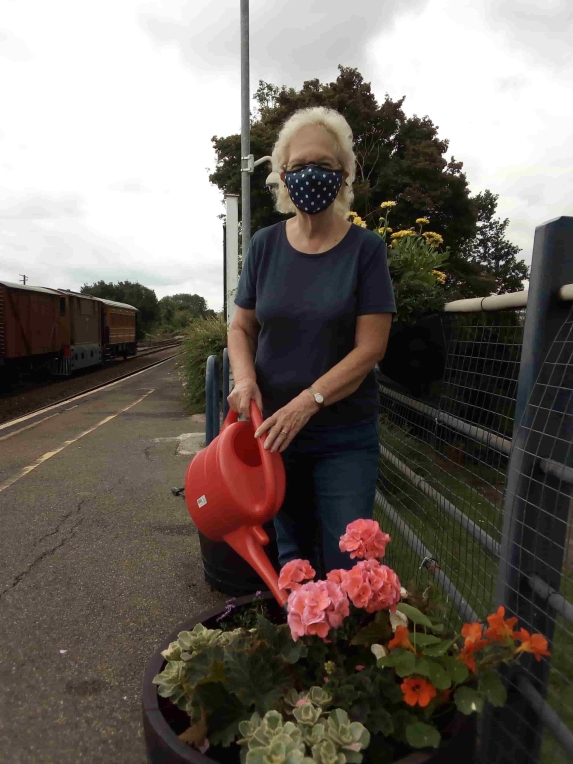 Woman wearing face covering and watering plants 