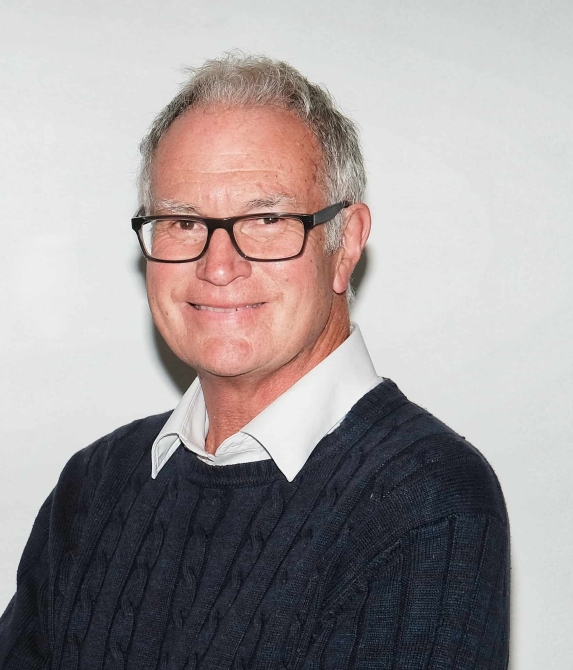 Man wearing a black jumper, shirt and glasses smiling