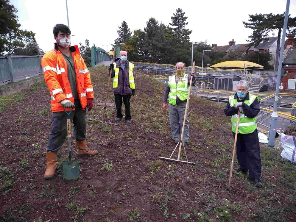 Volunteers in high visibility coats standing on Derby road pollinator patch