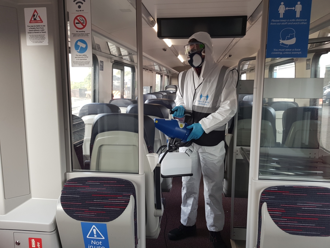 Man in white protective equipment, using fogging gun.